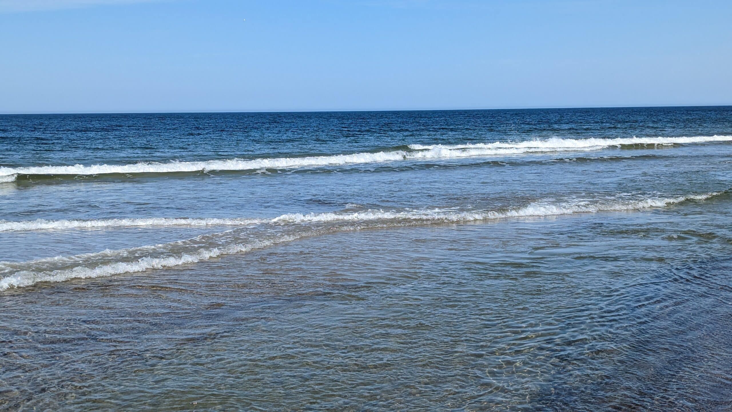 Ein Strand mit Wellen und Sand an einem sonnigen Tag.