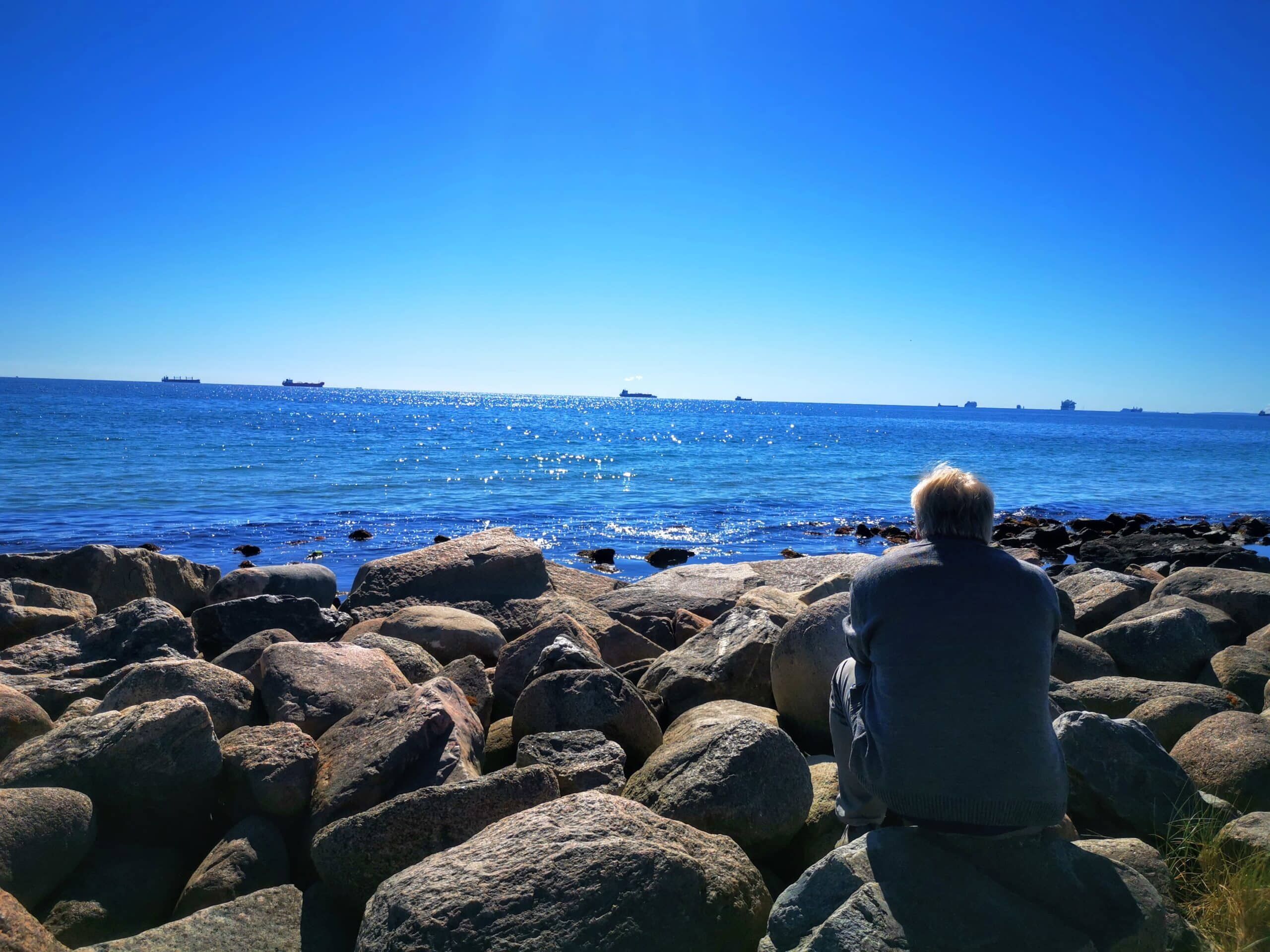 Ein Mann sitzt auf einem Felsen mit Blick auf den Ozean.