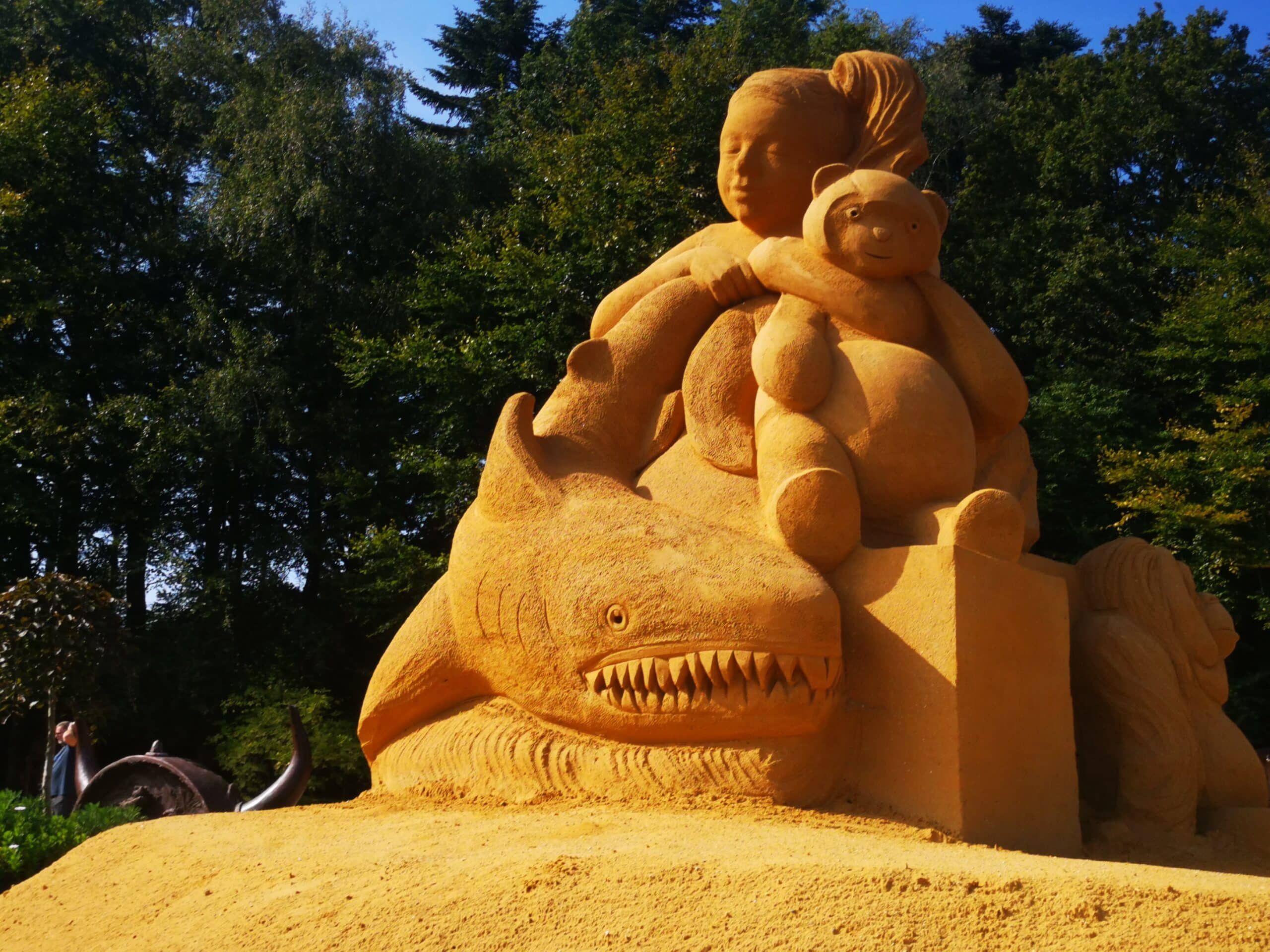 Eine Sandskulptur eines Kindes und eines Hais.