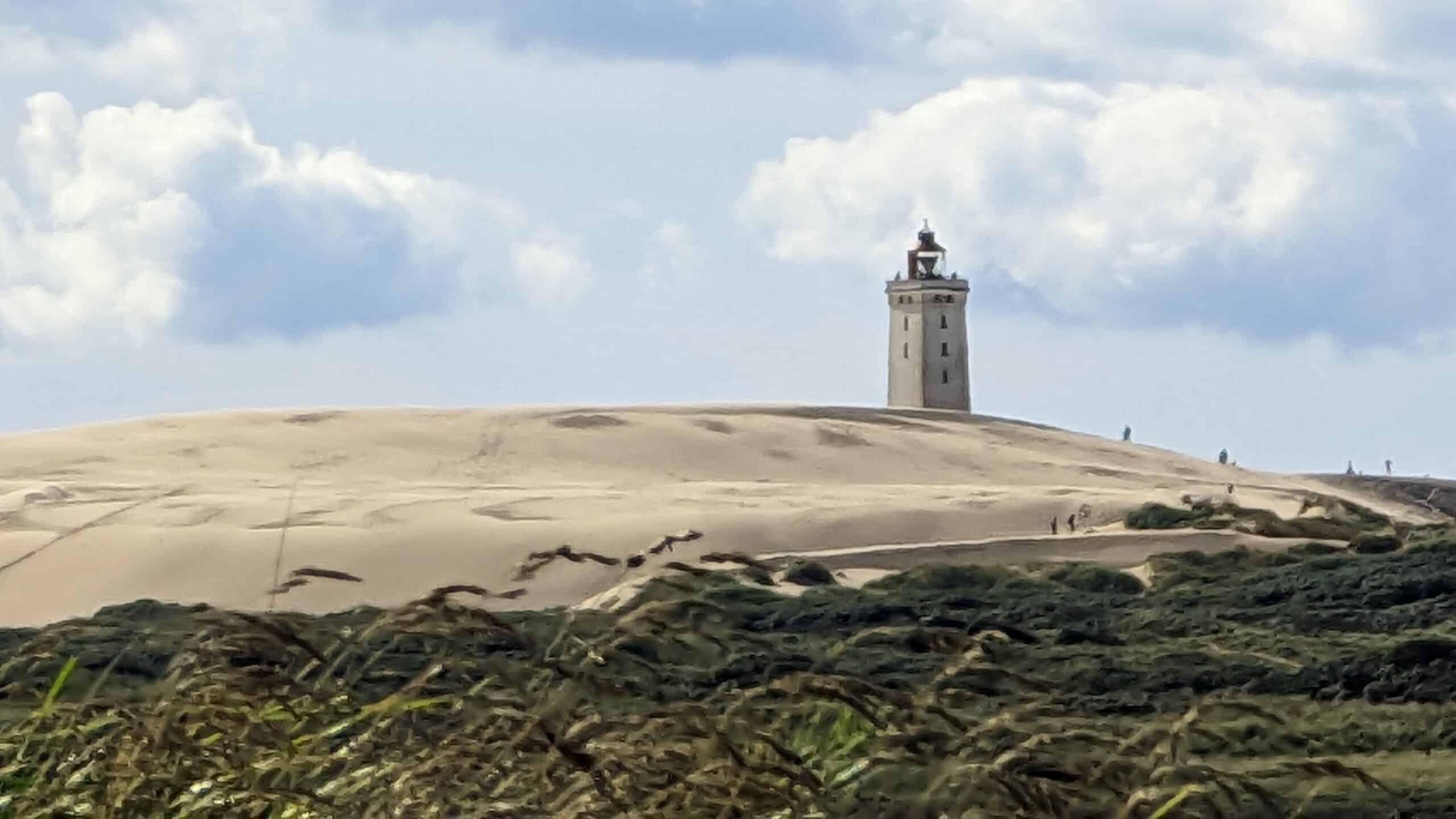 Ein Leuchtturm steht auf einer Sanddüne.