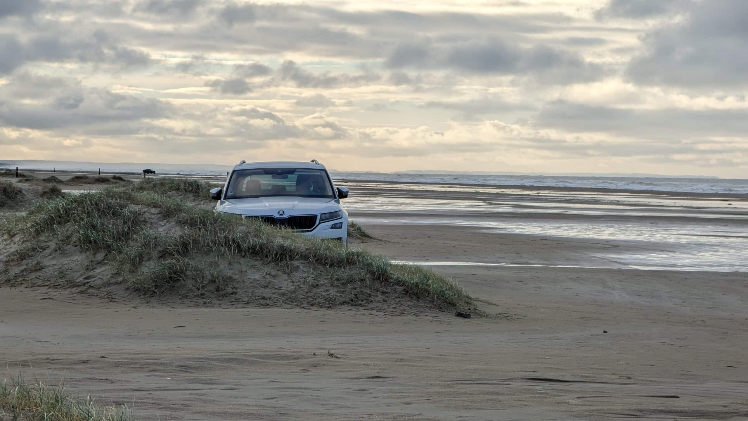 Ein weißer Geländewagen parkte in einer Sanddüne in der Nähe des Ozeans.