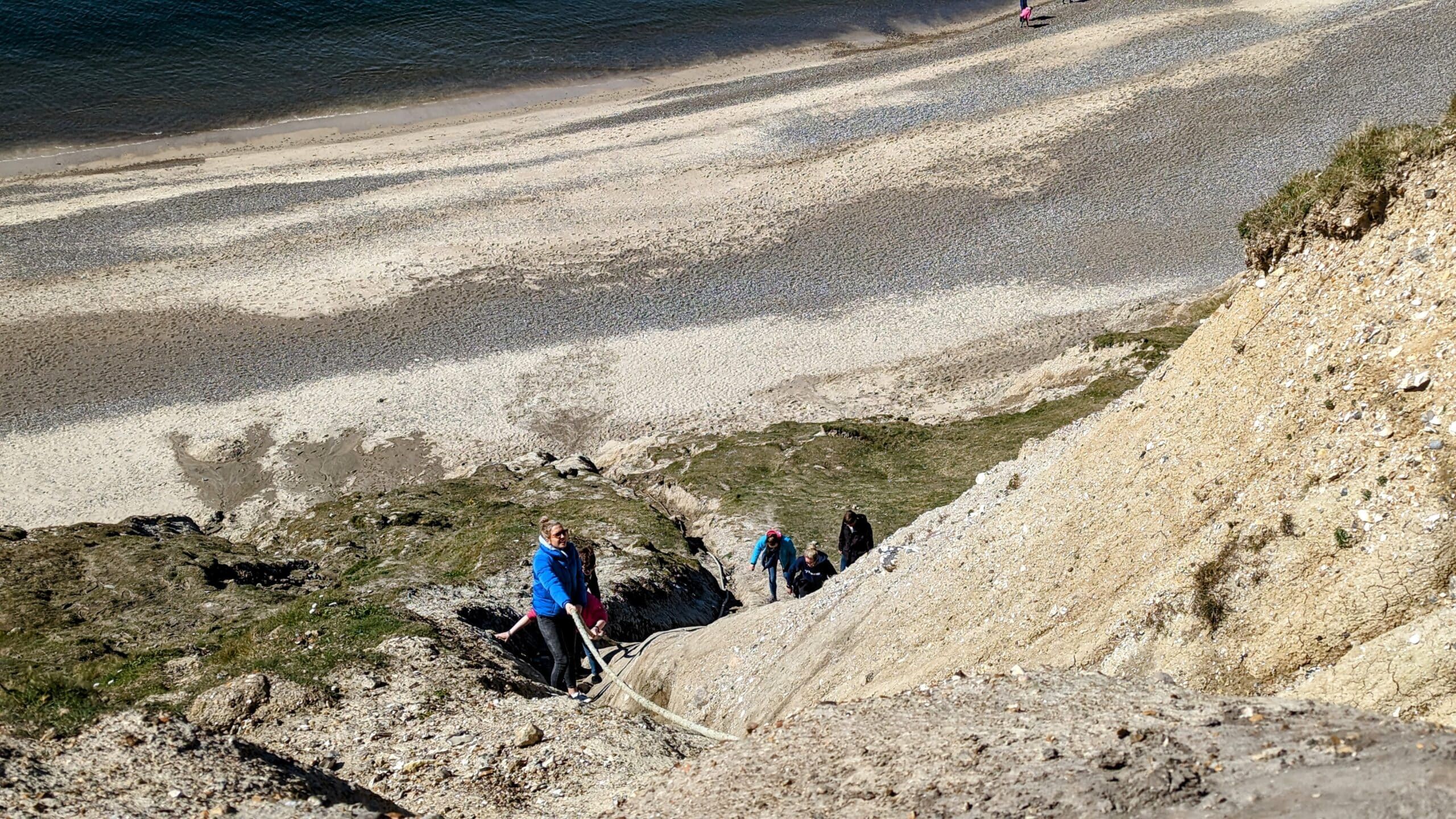 Eine Gruppe von Menschen geht eine felsige Klippe hinauf zum Strand.