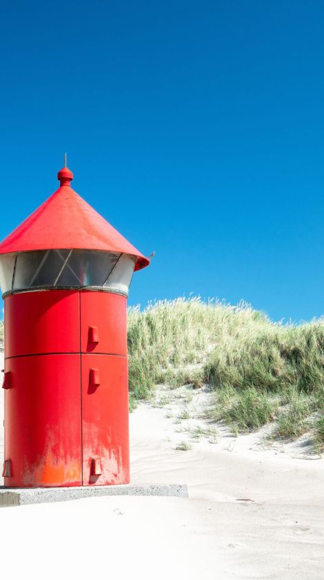 Ein roter Leuchtturm auf einer Sanddüne.