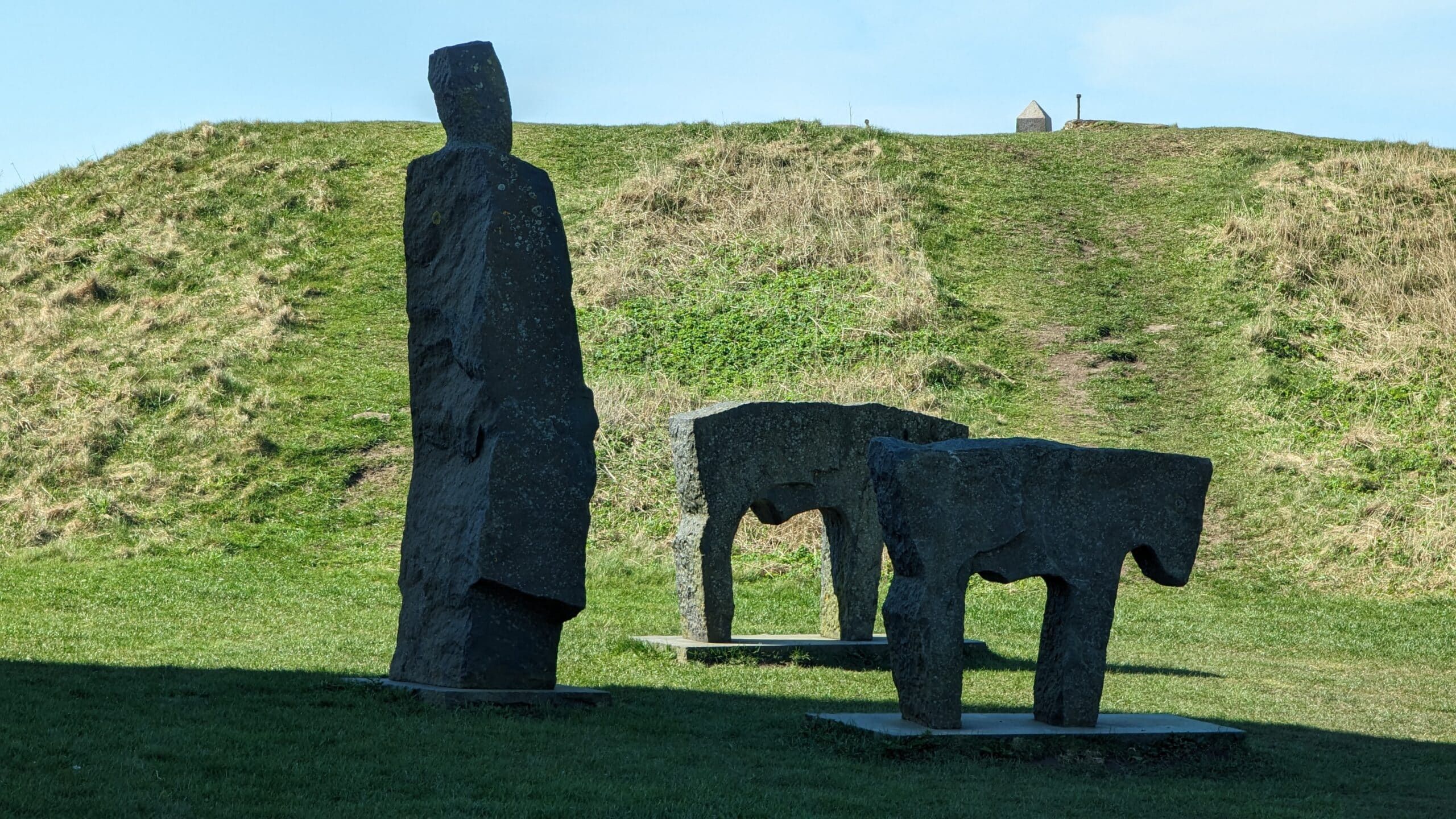 Drei Steinskulpturen auf einem grasbewachsenen Hügel.