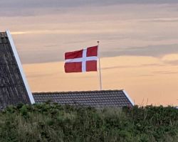 Eine dänische Flagge weht bei Sonnenuntergang über einem Haus.