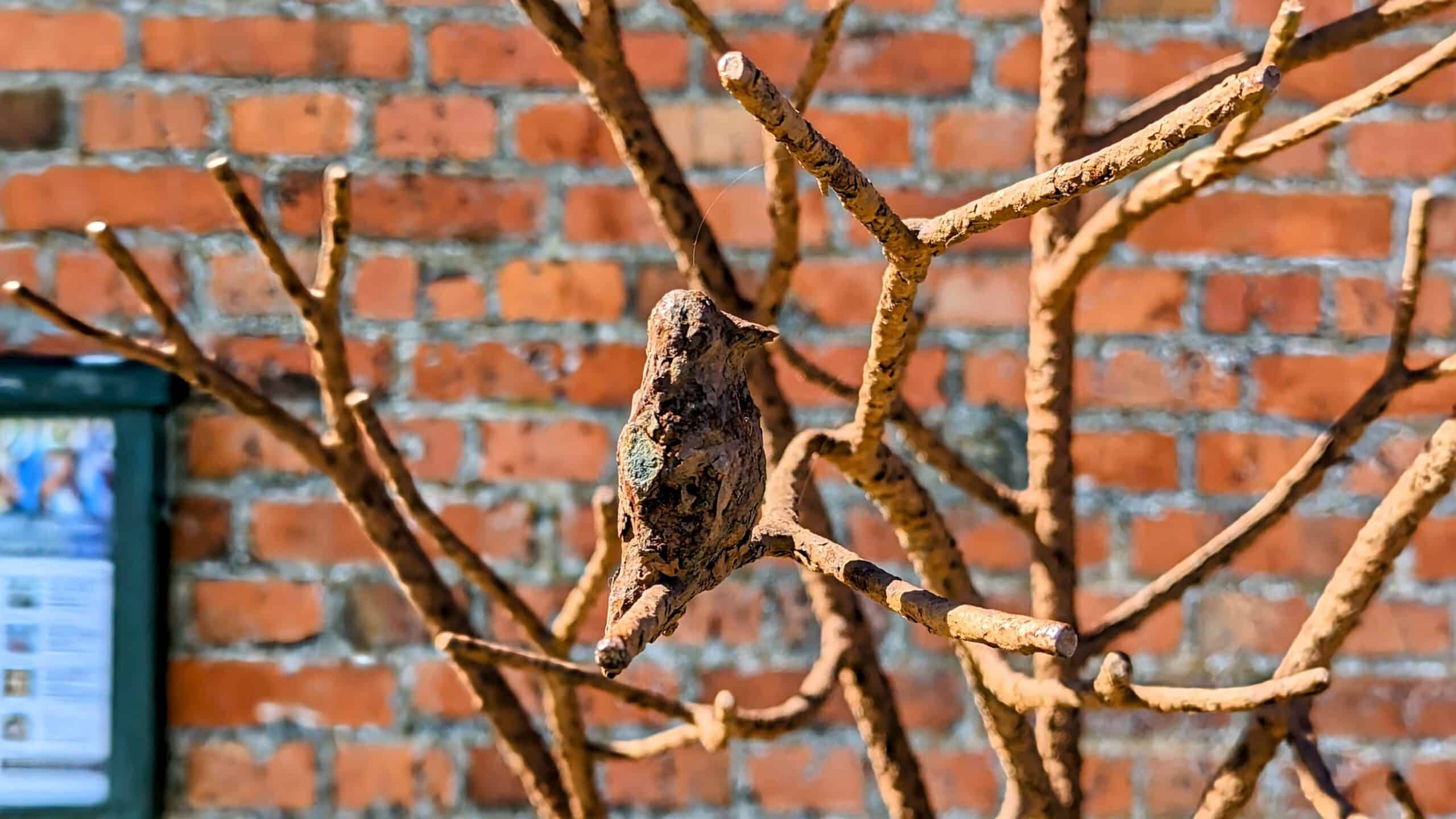Ein Vogel saß auf einem rostigen Ast vor einer Ziegelmauer.