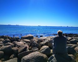 Ein Mann sitzt auf einem Felsen mit Blick auf den Ozean.