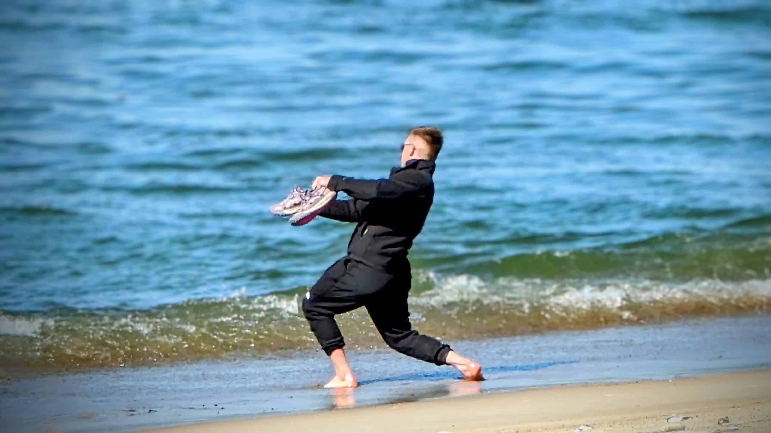 Ein Mann rennt mit einem Frisbee am Strand entlang.