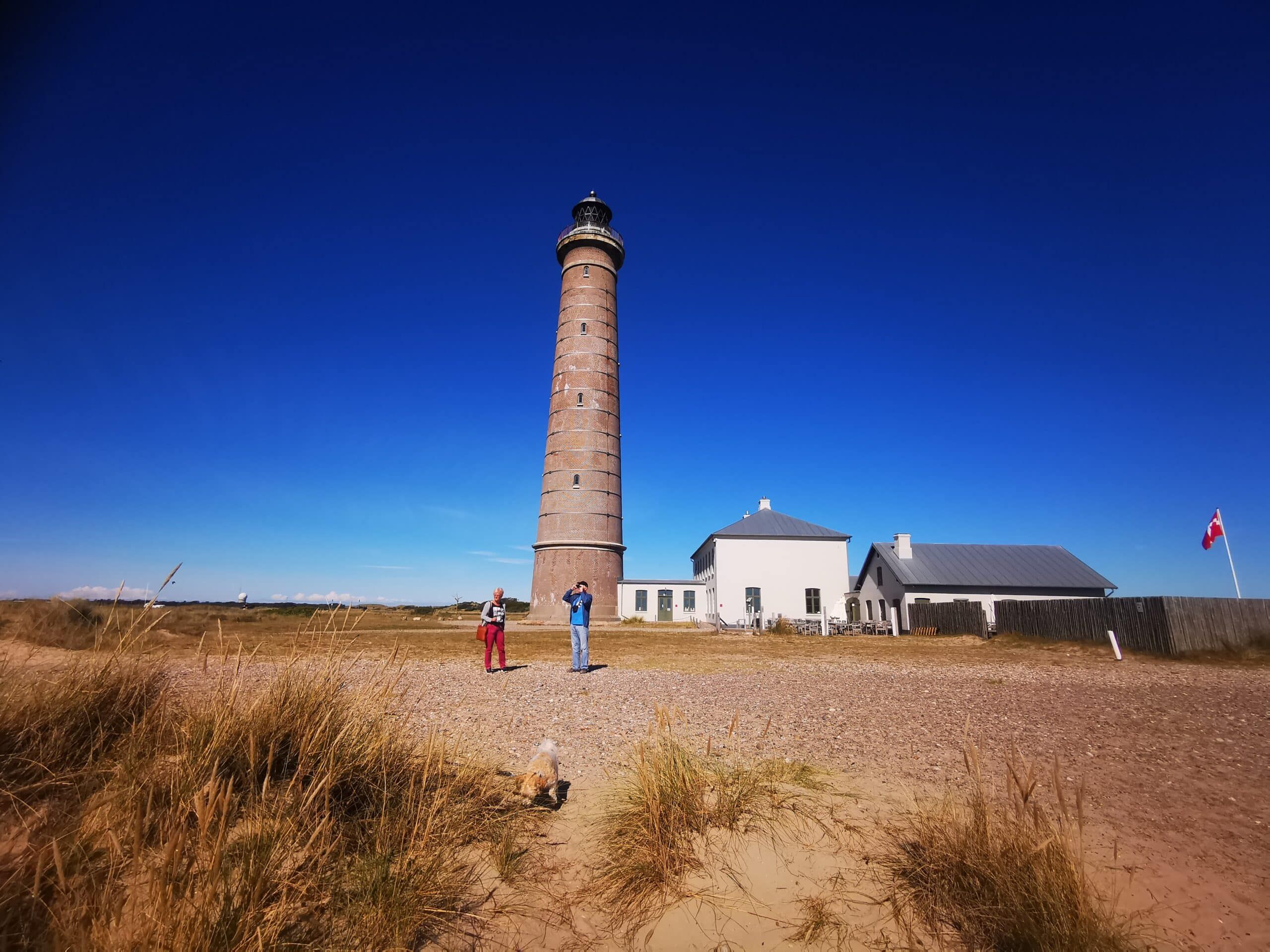 Zwei Personen stehen in der Nähe eines Leuchtturms im Sand.